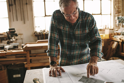 Carpenter studies the construction plan in his workshop