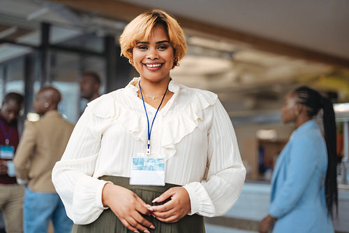 Young businesswoman smiling at a conference expo with colleagues in background