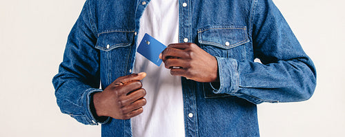 Man in a denim jacket pulls a credit card from his pocket in a studio setting