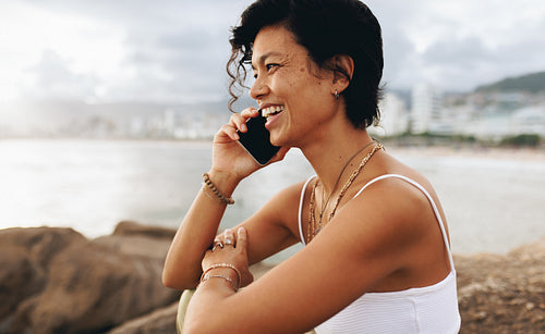 Smiling woman having a joyful conversation on her smartphone by the seaside