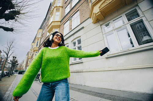The woman enjoys a city walk with headphones and music on her smartphone