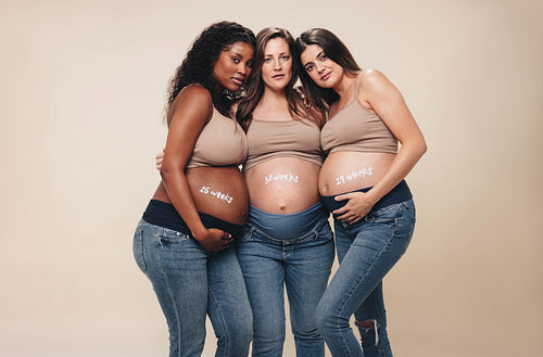 Multicultural group of pregnant women embracing their baby bumps in studio portrait