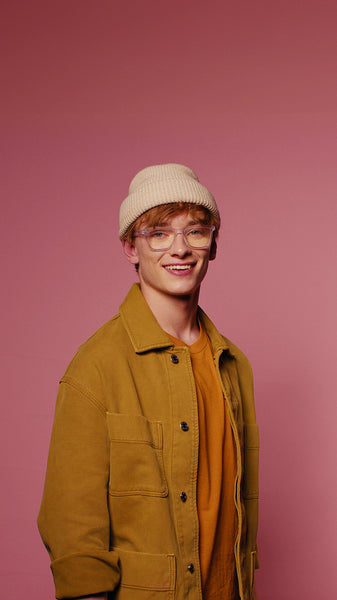 Smiling young man with glasses and beanie poses against a pink background