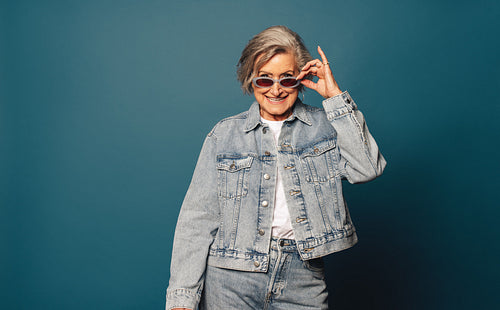 Cheerful senior peeking with denim and glasses on blue