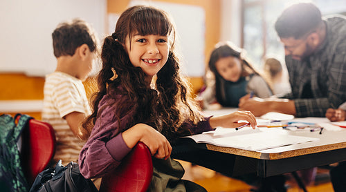 Girl smiling at the camera while sitting in an art and creativity class