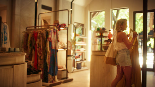 A happy woman trying on a stylish yellow dress in a bright luxury resort boutique