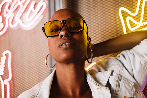 Woman in yellow sunglasses standing against a neon light background in a radio station