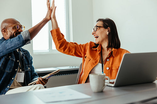 Team celebrating collaboration with a high-five in an office environment
