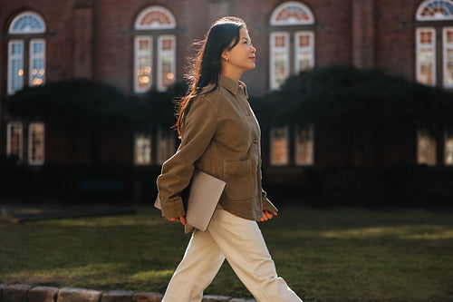 Woman walking across campus holding a laptop