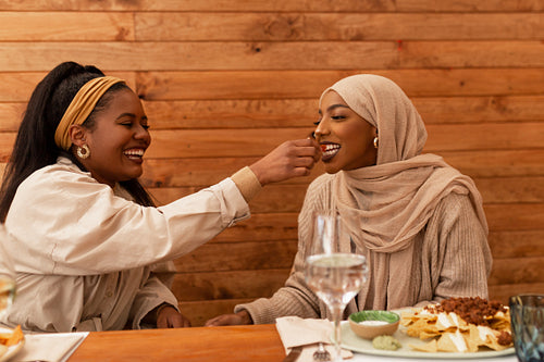 Happy young woman feeding her muslim best friend in a cafe