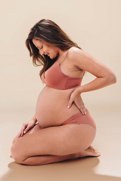 Maternal love: Pregnant woman smiling at her baby bump in a studio