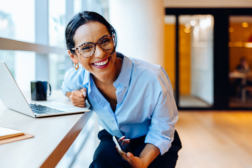 Smiling young woman with glasses working at a desk with a laptop