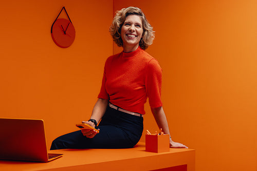 Happy mature woman smiling in a vibrant monochromatic orange office setting, conceptual studio portrait