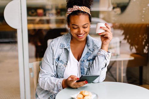 Smiling young woman enjoying coffee and using tablet in cafe