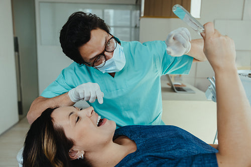 Dentist examining female patient's teeth with mirror in clinic