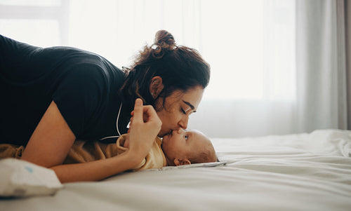 Mother kisses newborn baby on bed at home
