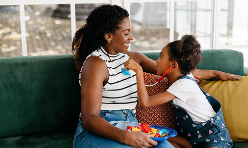 Mother and daughter enjoying doctor playtime together on a couch