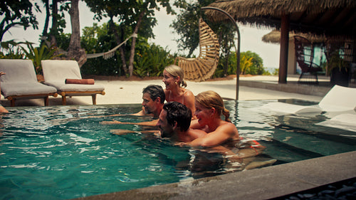Happy friends and family having fun with a piggyback race in a tropical resort pool