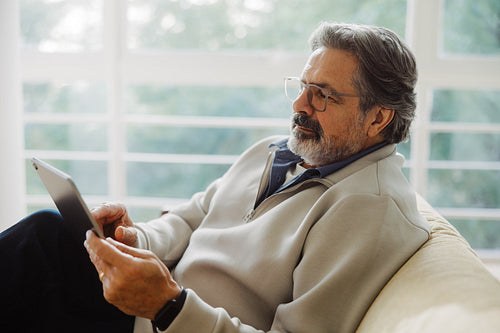 Senior man uses a tablet while sitting on a sofa at home