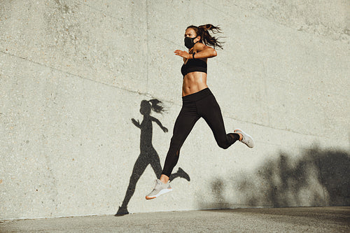 Athletic woman with face mask sprinting outdoors
