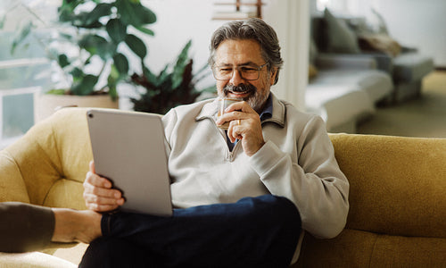 Senior man checks a tablet with coffee on the sofa