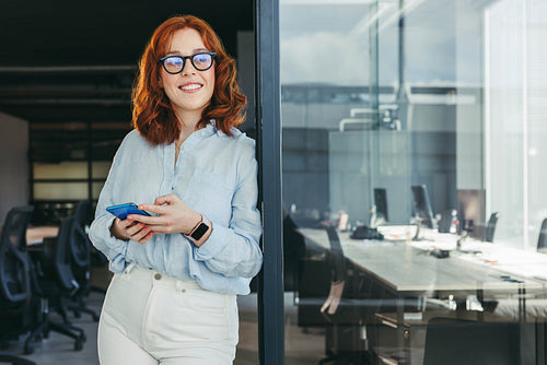 Professional businesswoman smiling and using her smartphone in a tech office