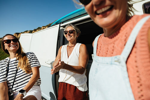 Three happy female friends enjoying a sunny holiday by their camper van