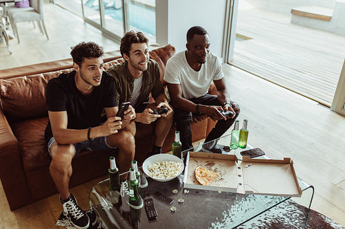 Top view of three friends playing a video game sitting at home