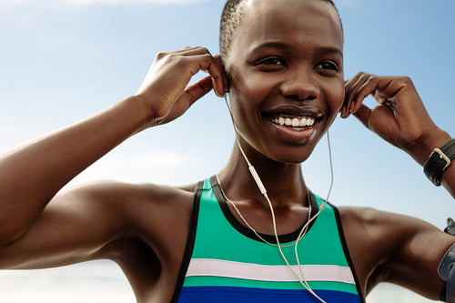 Smiling female runner adjusting her earphones