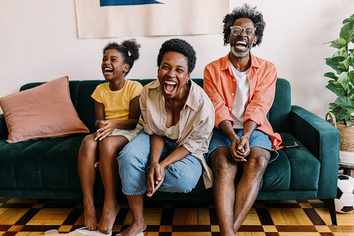 Family laughing happily while watching a football game at home