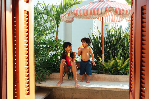 Latin American children enjoying ice pops on a sunny terrace by vibrant greenery