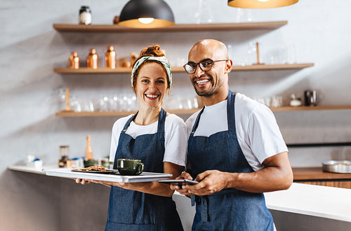 Two happy waiters standing together in a cafe, ready to serve customers