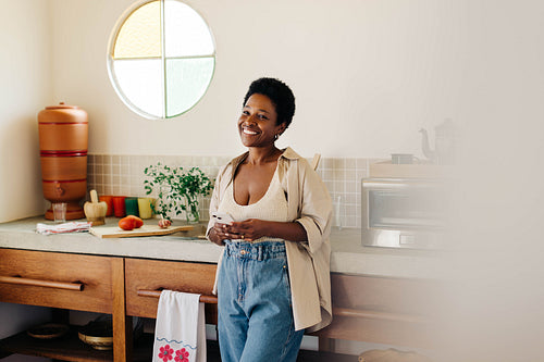 Brazilian woman smiling while using a smartphone in her kitchen