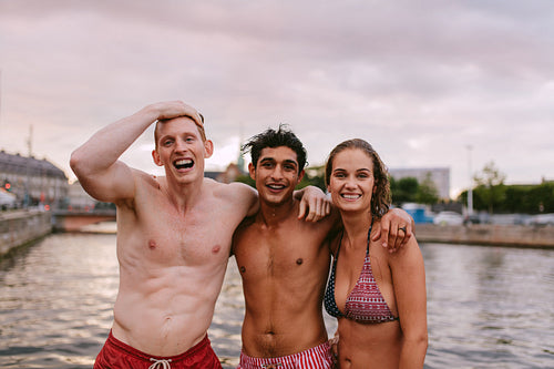 Friends in swimwear standing together by the lake