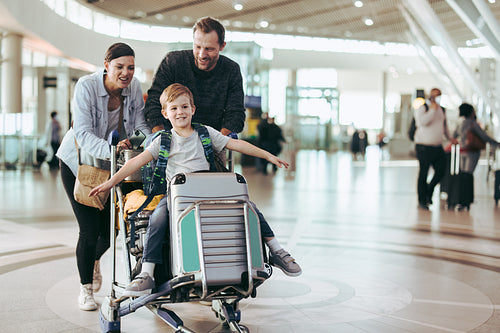 Parents pushing luggage trolley with their son at airport