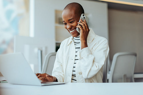 Young businesswoman working in office with laptop and smartphone, smiling and talking on the phone