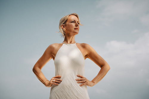Confident woman wearing elegant jewelry standing under a bright blue sky