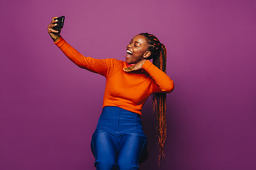 Happy girl with two tone braids taking selfie on colorful background.