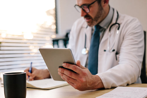 Doctor with digital tablet writing notes at his desk