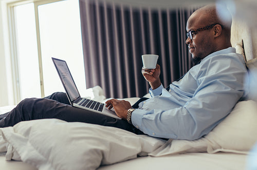Businessman working on laptop computer lying on bed
