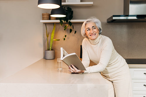 Senior woman looking away thoughtfully while holding a book