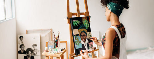 Young female painter working on a portrait painting in her studi