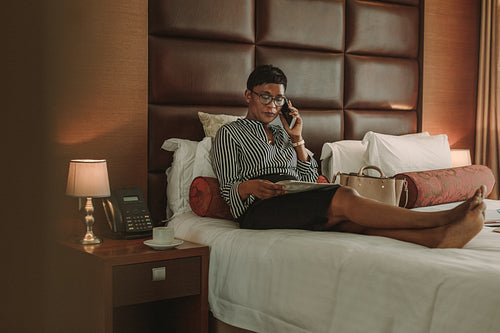 Businesswoman in hotel room with newspaper talking over phone