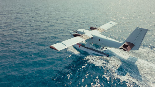 Seaplane taxiing on clear blue ocean water under bright sunny sky