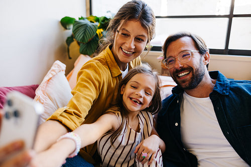 Family selfie: smiling parents with daughter at home