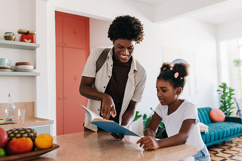Happy big brother helping his sister read a book in the morning at home