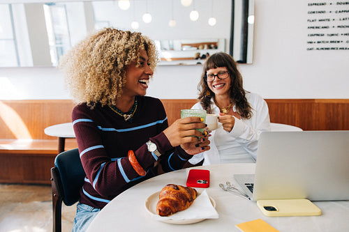 Friends laughing over coffee and laptop in cafe