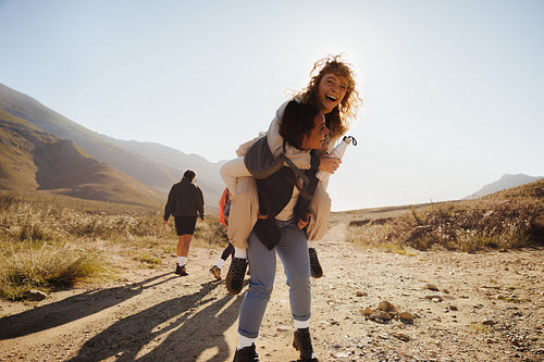 Friends laughing during piggyback ride on sunny mountain hike