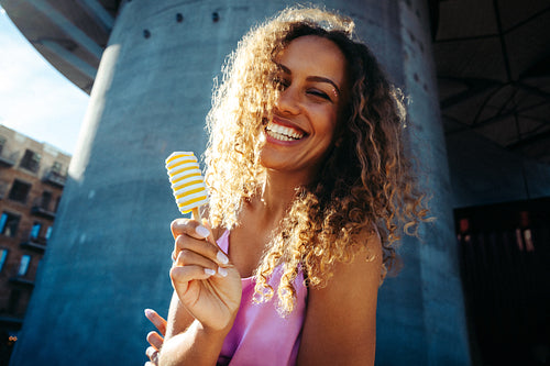 Woman licks a popsicle outdoors beneath an urban overpass in summer