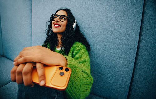 At home, the woman relaxes with headphones and a smartphone on the sofa